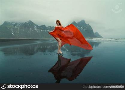 Attractive model in red dress on Reynisfjara beach scenic photography. Picture of person with hills on background. High quality wallpaper. Photo concept for ads, travel blog, magazine, article. Attractive model in red dress on Reynisfjara beach scenic photography