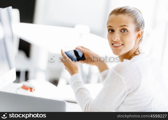 Attractive office worker sitting at desk. Attractive woman sitting at desk in office holding mobile phone