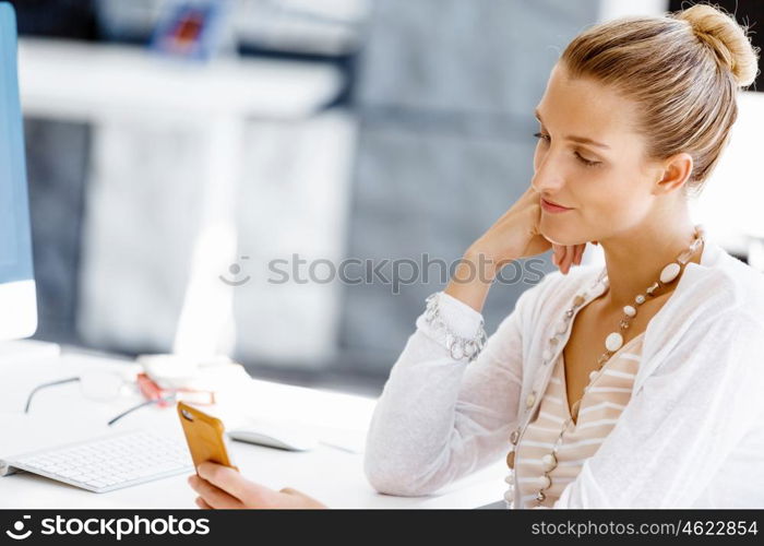 Attractive office worker sitting at desk. Attractive woman sitting at desk in office holding mobile phone