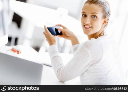 Attractive office worker sitting at desk. Attractive woman sitting at desk in office holding mobile phone