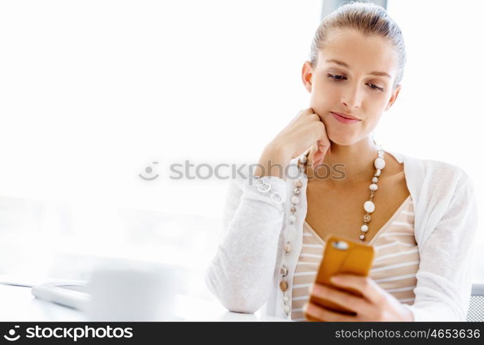 Attractive office worker sitting at desk. Attractive woman sitting at desk in office holding mobile phone