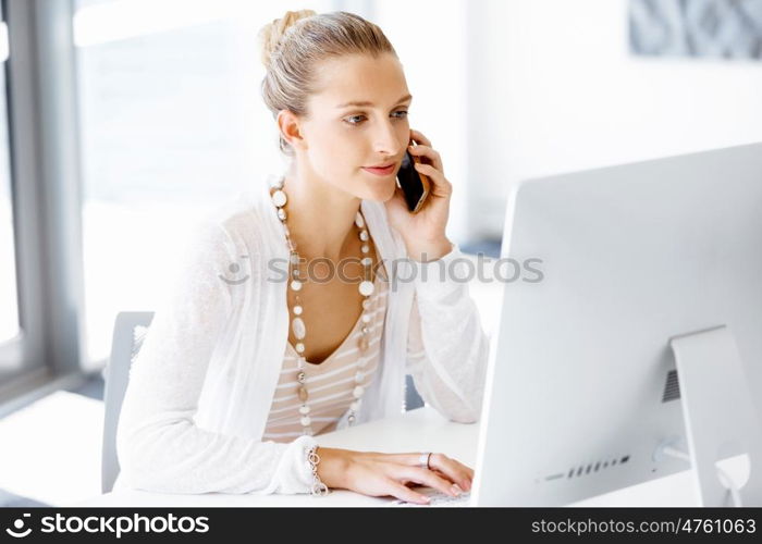 Attractive office worker sitting at desk. Attractive woman sitting at desk in office holding mobile phone