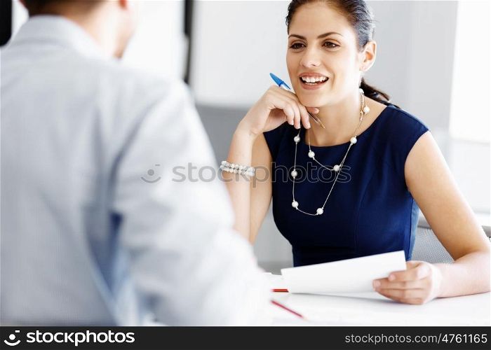 Attractive office worker sitting at desk. Attractive woman sitting at desk in office and talking to her colleague