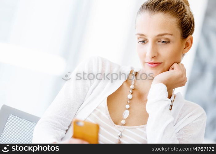 Attractive office worker sitting at desk. Attractive woman sitting at desk in office holding mobile phone