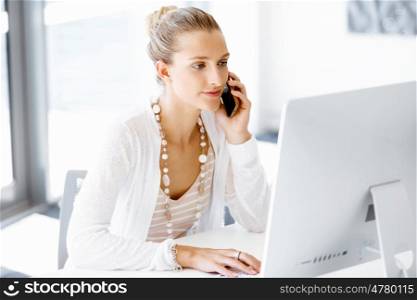 Attractive office worker sitting at desk. Attractive woman sitting at desk in office holding mobile phone