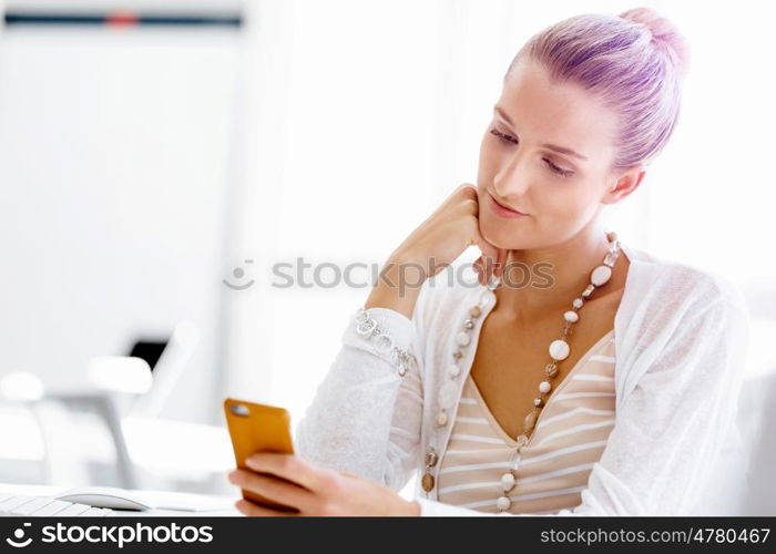 Attractive office worker sitting at desk. Attractive woman sitting at desk in office holding mobile phone