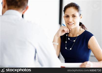 Attractive office worker sitting at desk. Attractive woman sitting at desk in office and talking to her colleague