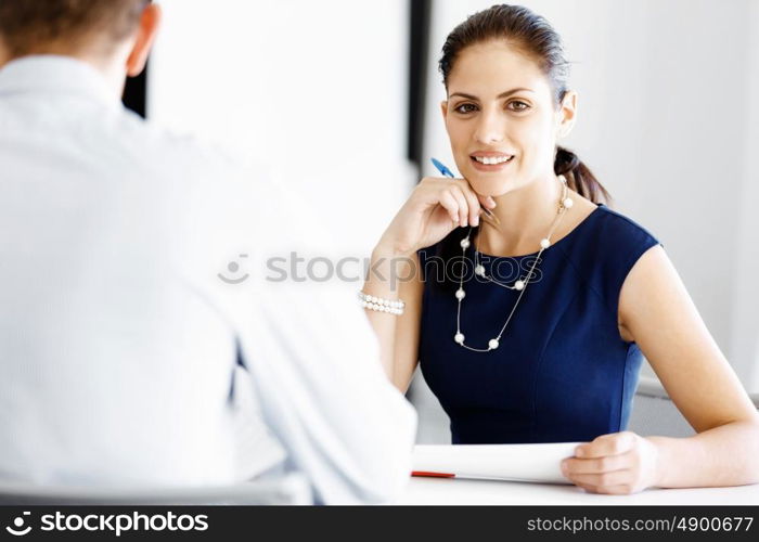 Attractive office worker sitting at desk. Attractive woman sitting at desk in office and talking to her colleague