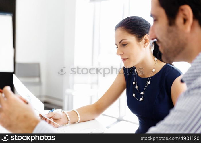 Attractive office worker sitting at desk. Attractive woman sitting at desk in office and talking to her colleague