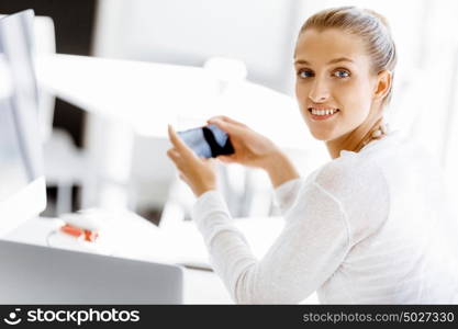 Attractive office worker sitting at desk. Attractive woman sitting at desk in office holding mobile phone