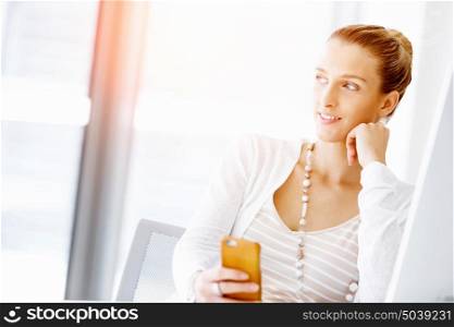 Attractive office worker sitting at desk. Attractive woman sitting at desk in office holding mobile phone