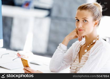 Attractive office worker sitting at desk. Attractive woman sitting at desk in office holding mobile phone