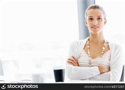 Attractive office worker sitting at desk. Attractive woman sitting at desk in office arms crossed