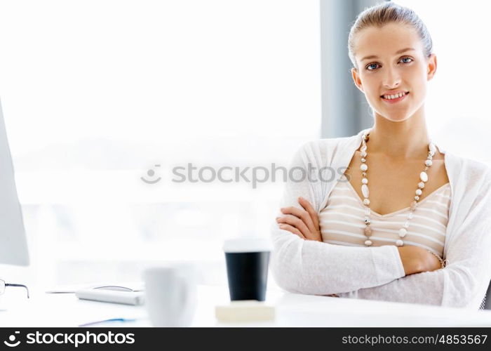 Attractive office worker sitting at desk. Attractive woman sitting at desk in office arms crossed