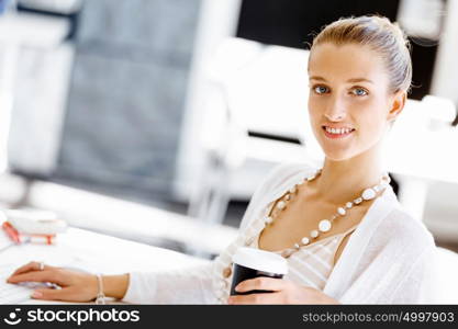 Attractive office worker sitting at desk. Attractive woman sitting at desk in office with coffee