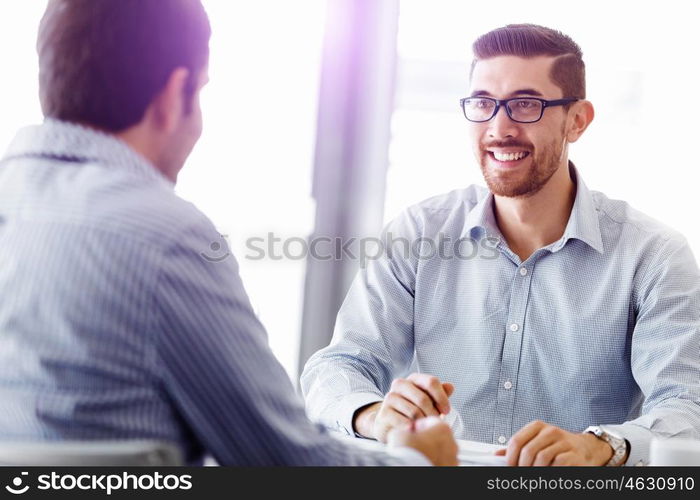 Attractive office worker sitting at desk. Young businessman sitting at desk in office and talking to his colleague