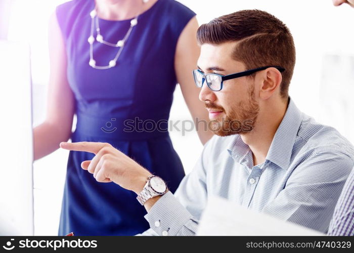 Attractive office worker sitting at desk. Young businessman sitting at desk in office and talking to his colleagues