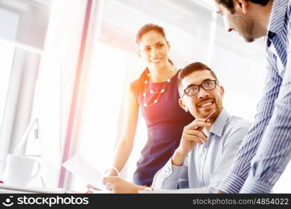 Attractive office worker sitting at desk. Young businessman sitting at desk in office and talking to his colleagues