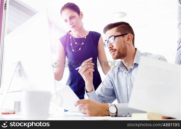 Attractive office worker sitting at desk. Young businessman sitting at desk in office and talking to his colleagues