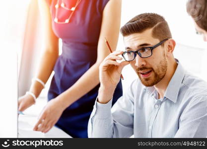 Attractive office worker sitting at desk. Young businessman sitting at desk in office and talking to his colleagues