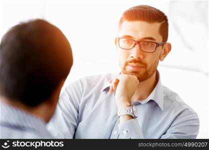 Attractive office worker sitting at desk. Young businessman sitting at desk in office and talking to his colleague