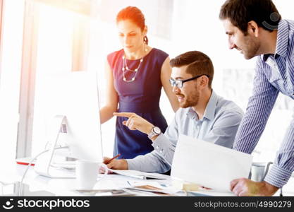 Attractive office worker sitting at desk. Young businessman sitting at desk in office and talking to his colleagues