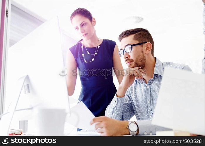 Attractive office worker sitting at desk. Young businessman sitting at desk in office and talking to his colleagues