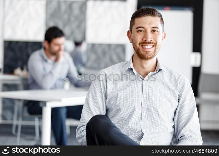 Attractive office worker sitting at desk. Young businessman sitting at desk in office