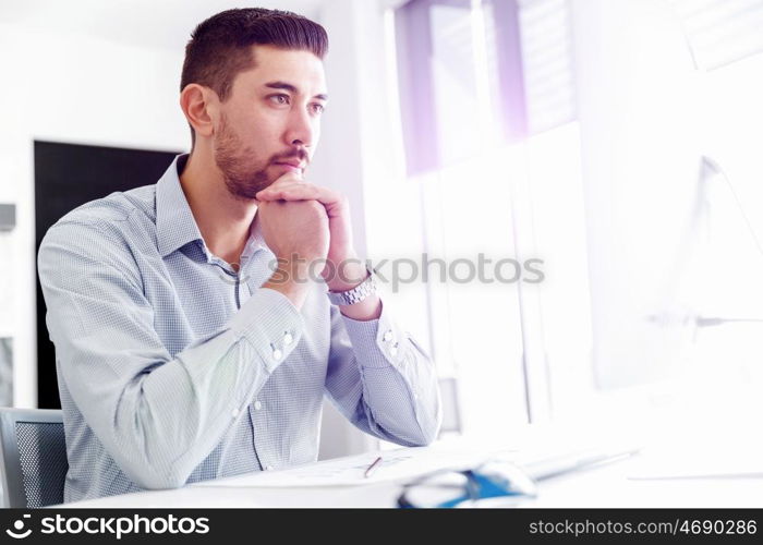 Attractive office worker sitting at desk. Young businessman sitting at desk in office