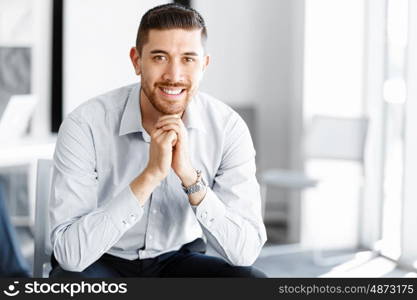 Attractive office worker sitting at desk. Young businessman sitting at desk in office