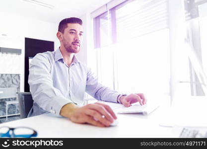 Attractive office worker sitting at desk. Young businessman sitting at desk in office