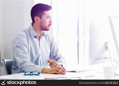 Attractive office worker sitting at desk. Young businessman sitting at desk in office