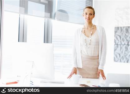 Attractive office worker standing next to window. Attractive woman sitting in office standing next to window