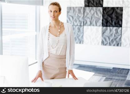 Attractive office worker standing next to window. Attractive woman sitting in office standing next to window