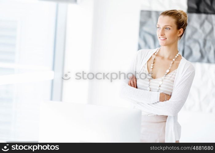 Attractive office worker standing next to window. Attractive woman sitting in office standing next to window