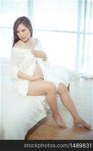 Attractive pregnant asian woman in bed and holding her belly