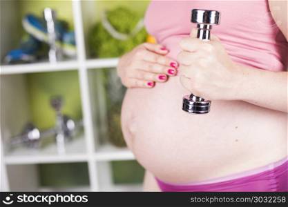 Attractive pregnant woman using a dumbbell while training. Fitness Pregnancy woman, healthy lifestyle concept