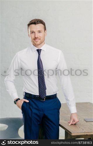 Attractive prosperous male in formal clothes, poses in office building, works on new businnes project. Successful man manager being at work place. Entrepreneur develops new idea for success.