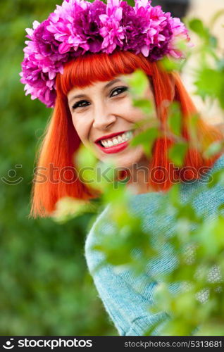 Attractive red haired girl with wreath of flowers in a park