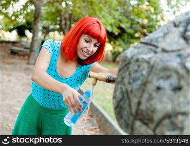 Attractive redhead girl filling a bottle of water in a fountain