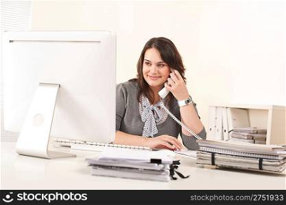 Attractive secretary on phone at office in front of computer screen