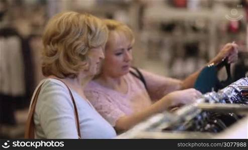 Attractive senior ladies selecting new apparel and looking through hangers with different casual garments in clothing store. Elderly women shopping at garments fashion shop.