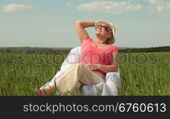 Attractive senior woman relaxing on green meadow, medium shot