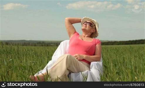 Attractive senior woman relaxing on green meadow, medium shot