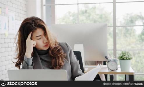 Attractive smart Asian business woman in smart casual wear working on laptop while sitting on desk while her angry manager standing angry throwing papers on office desk. Women work at office concept.