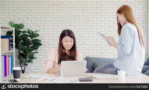 Attractive smart creative Asian business women in smart casual wear working on laptop while sitting on desk on office desk. Women work at office concept.