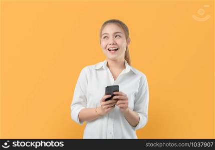 Attractive smiling Asian woman holding smartphone isolated on light orange background.
