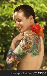 Attractive smiling Caucasian tattooed woman with Hibiscus flower over her shoulder in Maui, Hawaii, USA.