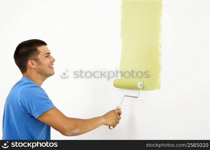 Attractive smiling man painting white wall with green paint.