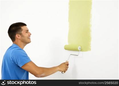 Attractive smiling man painting white wall with green paint.